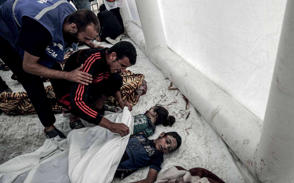 في مستشفى الشفاء، يقف فلسطيني بجوار جثث أطفاله الذين قُتلوا في هجمات الجيش الإسرائيلي.